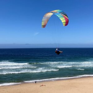 A vibrant BGD Cure paraglider with enzyme colors soaring gracefully against a clear blue sky, symbolizing the thrill of paragliding adventures.