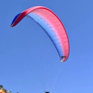 A vibrant image showcasing the UP Meru paraglider, size L, against a backdrop of blue skies. The glider is neatly packed with a brand-new concertina and rucksack beside it, ready for an exhilarating flight.