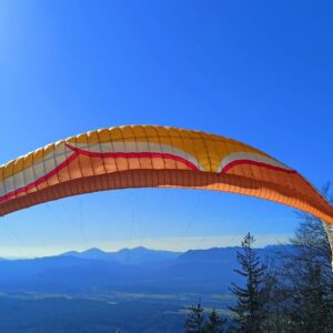 A vibrant orange and white Ozone Zeolite GT paraglider soaring high against a clear blue sky.