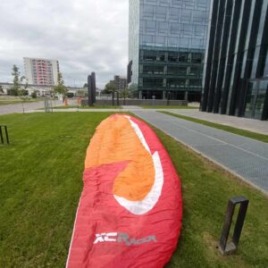 Front page image of a Flow XC Racer paraglider in vibrant red, white, and orange colors, for sale with only 60 hours of use, weight range 95-115 kg, EN D certification, located in Bucharest, Romania.