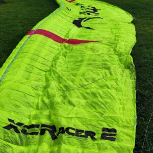 A nearly mint Flow XC Racer 2 paraglider in lime green, size L, with a weight range of 110-125 kg, displayed neatly with its concertina bag.