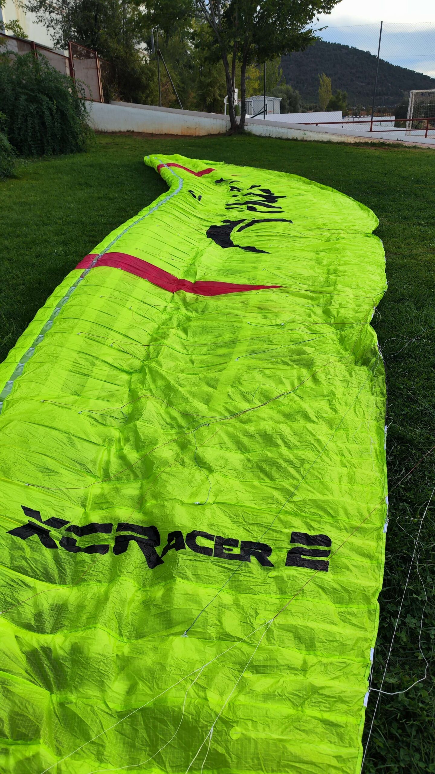 A nearly mint Flow XC Racer 2 paraglider in lime green, size L, with a weight range of 110-125 kg, displayed neatly with its concertina bag.