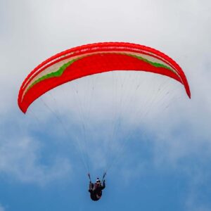 Gin Atlas XS paraglider in red, green, and white colors, suitable for light-weight pilots and girls, photographed outdoors on grassy terrain