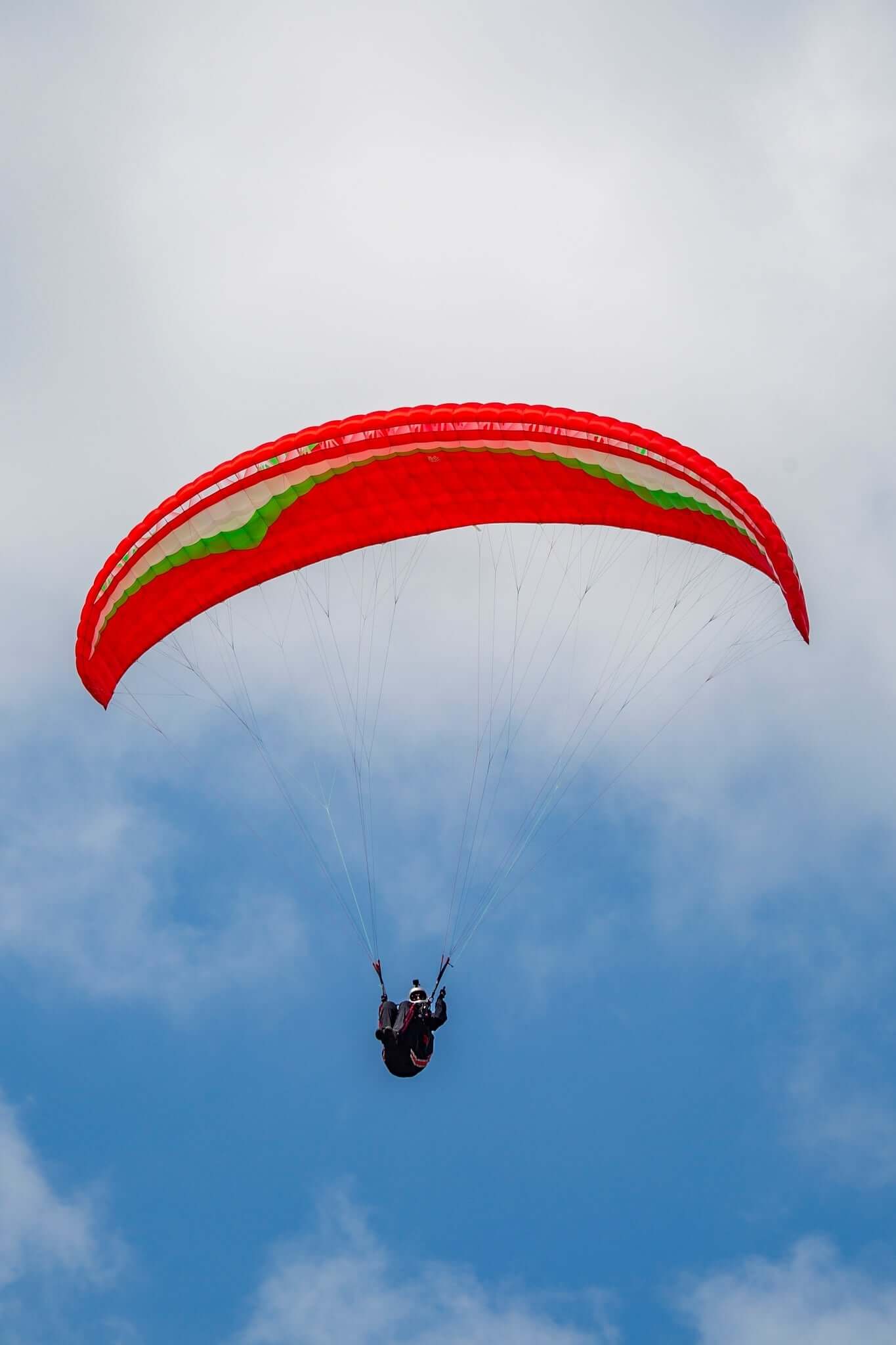 Gin Atlas XS paraglider in red, green, and white colors, suitable for light-weight pilots and girls, photographed outdoors on grassy terrain
