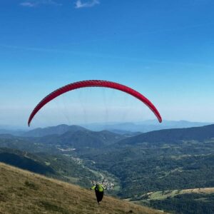 Red Ozone Alpina 4 paraglider neatly packed on a grassy field, showcasing ultralight fabric and compact concertina bag