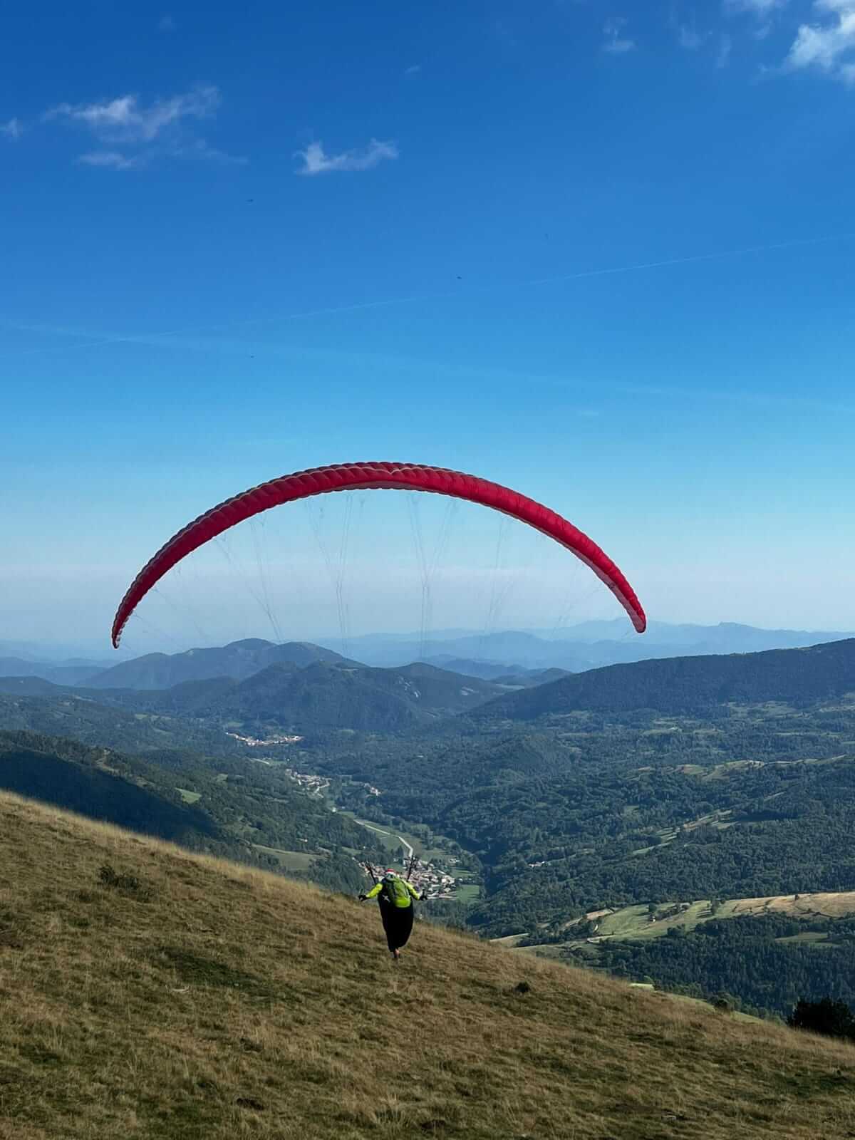 Red Ozone Alpina 4 paraglider neatly packed on a grassy field, showcasing ultralight fabric and compact concertina bag